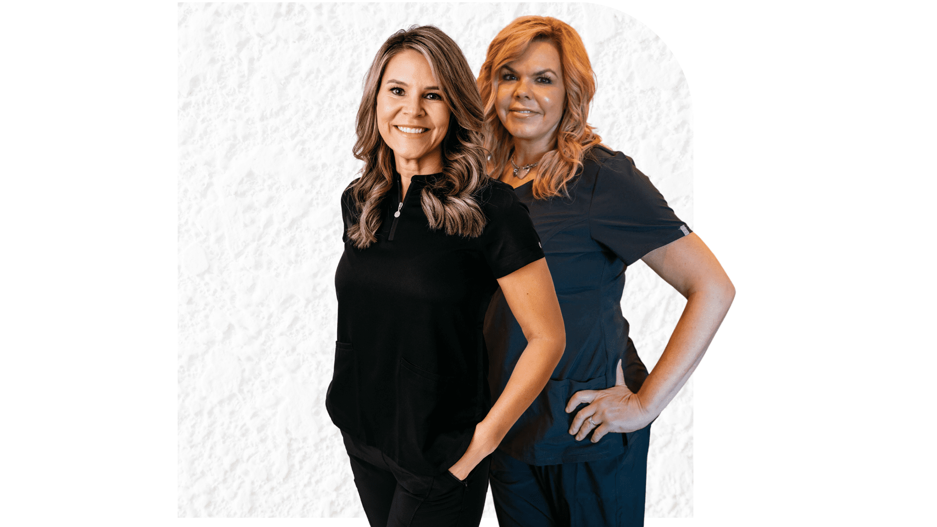 Two smiling women wearing dark medical scrubs