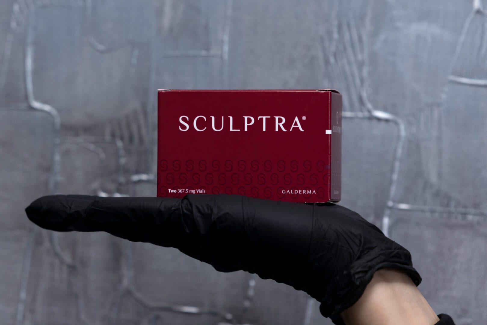 Gloved hand holding red Sculptra box