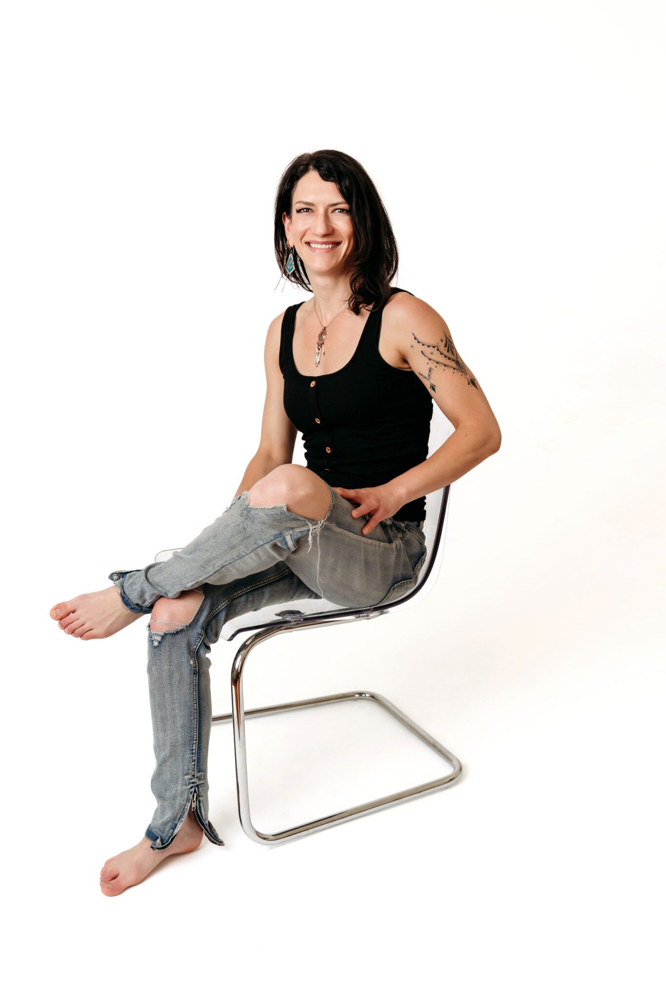 Woman in ripped jeans seated barefoot on chair